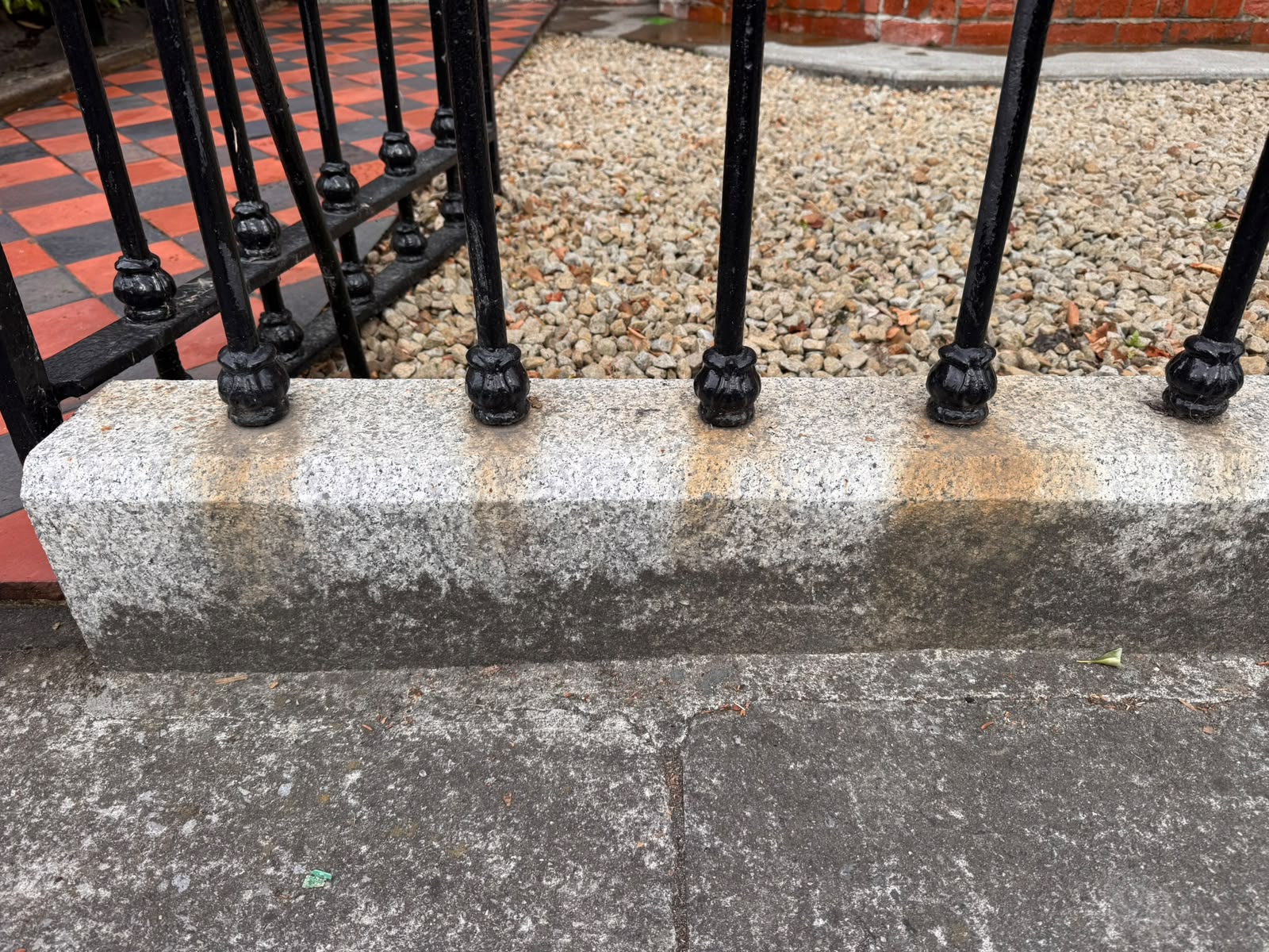 Granite plinth beneath cast iron railings before cleaning — heavy rust staining and algae growth